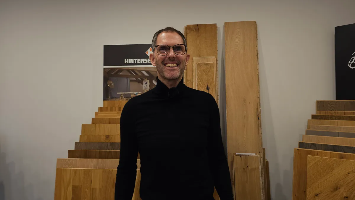 Andre Ruschitzka vor Holzmustern in der Ausstellung — Eiche, Räuchereiche, Nussbaum