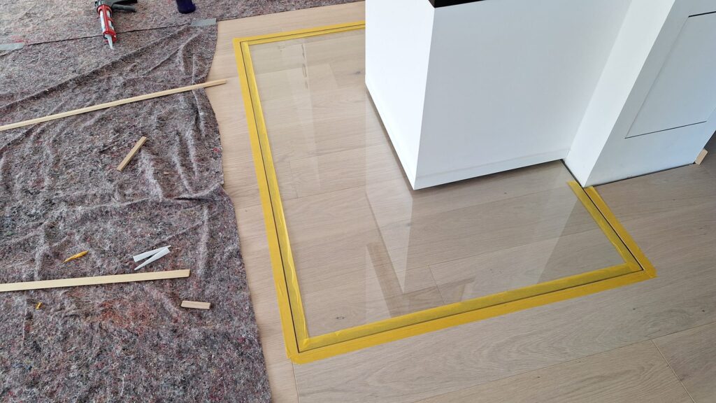 Passgenau eingesetzte Glasscheibe, mit gelbem Klebeband für eine saubere Silikonfuge vorbereitet.